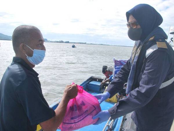 Kepten Zulinda (kanan) menyerahkan sumbangan barangan keperluan asas kepada Rashid yang berada atas bot nelayan berhampiran Pulau Ketam di sini hari ini.