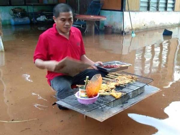 Mohd Razak membakar ayam percik bagi juadah berbuka puasa di laman rumahnya yang dinaiki air semalam.