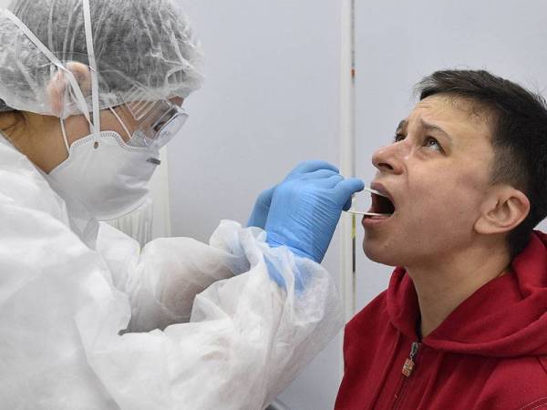 Seorang kakitangan perubatan mengambil sampel daripada seorang individu di kemudahan ujian pandu masuk Covid-19 di Moscow. - FOTO: AFP