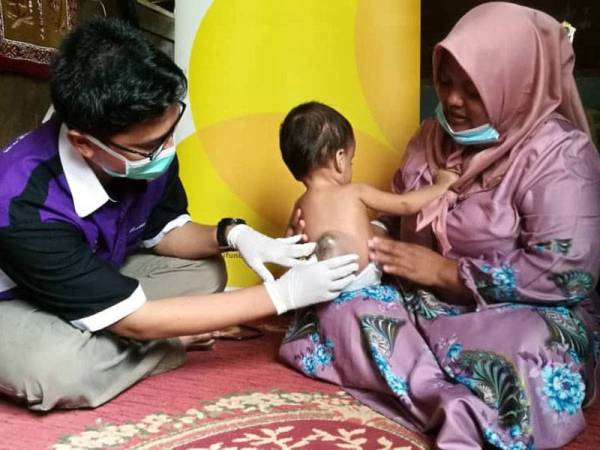 Dr Ahmad Luqman memeriksa belakang Muhammad Wasir sambil diperhatikan Mariana ketika menziarahi bayi tersebut di rumahnya, di Kampung Sadang, Belanja Kiri di sini hari ini.