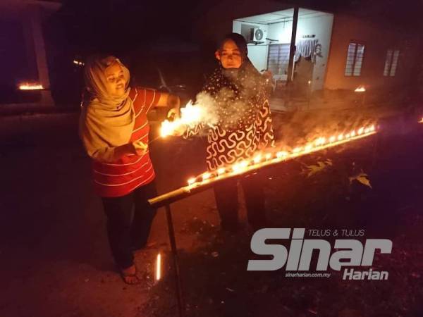 Kamsiah menemani anak sulungnya bermain bunga api dengan menggunakan pelita buluh di rumahnya di Kampung Belimbing Dalam.