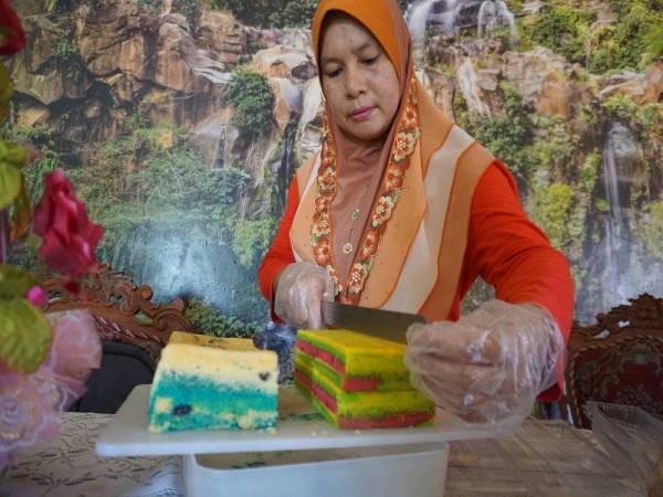 Rajemah Rose Awi memotong kek lapis masam manis yang ditempah pelanggan ketika tinjauan di rumahnya di Kampung Bubor, di sini. - Foto Bernama