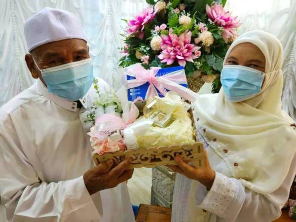 Yaakob dan Saudah menunjukkan topeng muka dan cecair pembasmi kuman yang dijadikan sebagai hantaran pada majlis perkahwinan mereka.