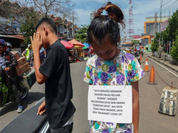 Seorang pelaku yang ditahan melanggar langkah PSBB memakai plakad tertera ‘saya berjanji akan memakai topeng muka’ yang turut dimuat naik di media sosial. - FOTO: AFP