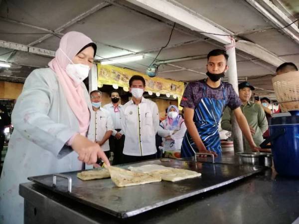 Zuraida membantu seorang penjual roti canai, Mohammad Amirul Abd Latif, 25, dalam lawatannya ke Gerai Rakyat di pekan Langkap di sini hari ini.