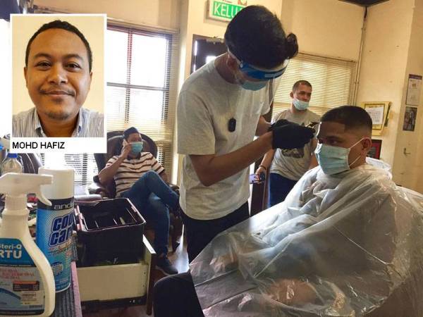 Pekerja Gunteng Barber Shopmemastikan kelengkapan keselamatan dipakai sebelum menggunting rambut pelanggan.