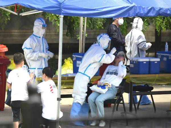 Pekerja kesihatan melakukan ujian swab ke atas seorang wanita di Beijing selepas program ujian besar-besaran dilancarkan. - Foto AFP