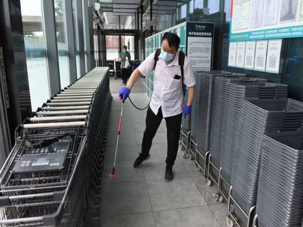 Seorang kakitangan melakukan semburan nyahjangkit di pintu masuk sebuah pasar raya di Beijing. - Foto AFP