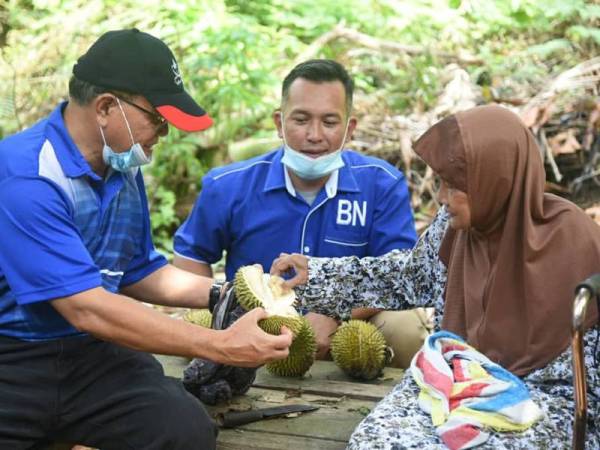 Wan Rosdy (kanan) bersama Mohd Sharim (tengah) meluangkan masa menikmati buah durian pada program ziarah sempena PRK Chini di Kampung Salong hari ini.