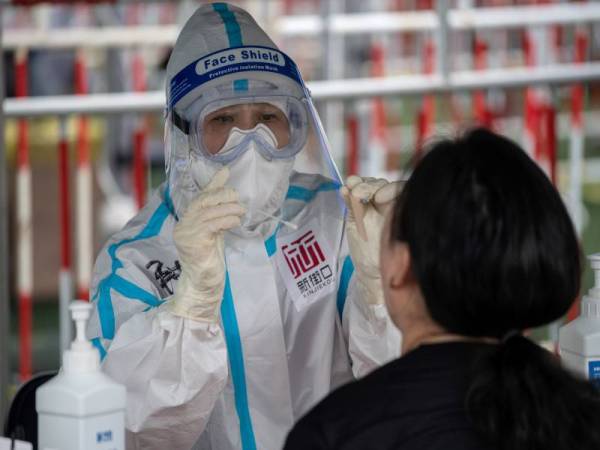 Seorang pekerja kesihatan melakukan ujian swab pada seorang wanita ketika ujian Covid-19 besar-besaran di Beijing hari ini. - Foto AFP