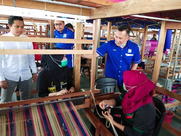 Mohd Sharim (dua dari kiri) meninjau kerja-kerja menenun yang dilakukan pekerja di Pusat Tenun Pahang Diraja Felda di Chini semalam.