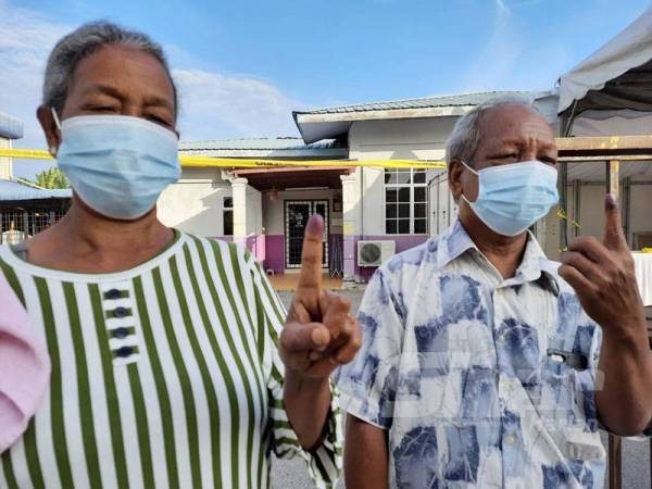 Ku Yu (kanan) bersama isterinya, Beriah menunjuk jari yang dicalit dakwat biru sebagai tanda selesai mengundi di pusat pengundian di Dewan Mempelas, Kampung Salong hari ini.