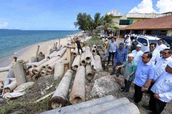 Tuan Ibrahim (tiga, kanan) melihat benteng pemecah ombak yang dibina sendiri penduduk selepas hakisan pantai di Pantai Rusila hari ini.