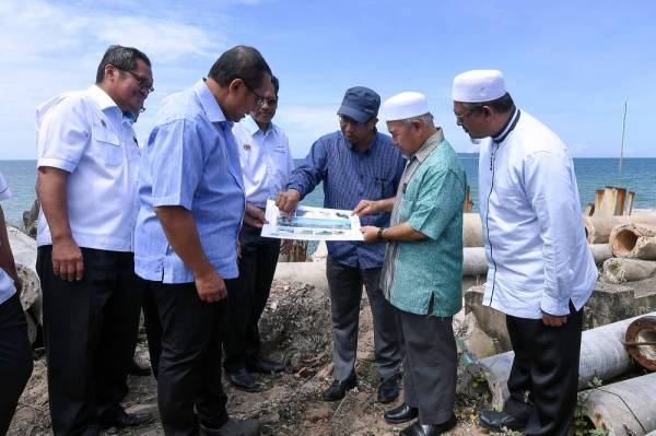 Tuan Ibrahim (baju hijau) dan Ahmad Samsuri (dua dari kiri) melihat pelan perancangan membina benteng pemecah ombak di Pantai Rusila, Marang hari ini.