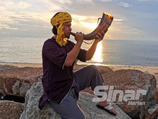 Mohd Azwarin meniup tetuang yang dihasilkan daripada tanduk kerbau balau ketika matahari naik sekitar jam 7 pagi di pantai Mengabang Telipot, Kuala Nerus. - Foto NORHASPIDA YATIM