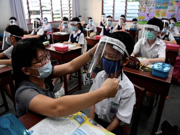 Guru kelas darjah 5B SJKC Jelutong, Ong Ai Hoon (kiri) membantu muridnya Ong Kai Jun,11, memakai 'face sheild' dengan betul ketika memulakan hari pertama pesekolahan dengan norma baharu ketika tinjauan di sekolah tersebut hari ini. - Foto Bernama