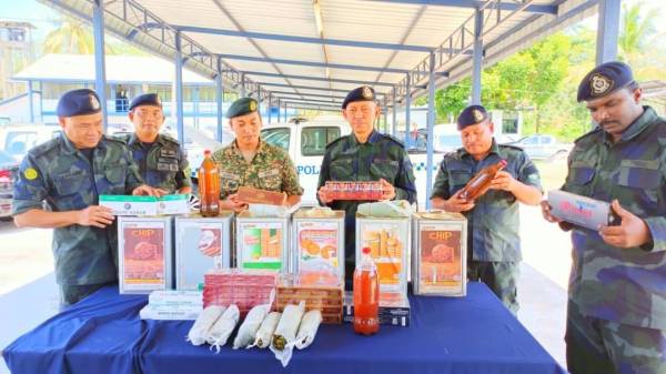 Hasan Basri (tiga,kanan) bersama Azhari (kiri) menunjukkan tin biskut yang digunakan penyeludup.