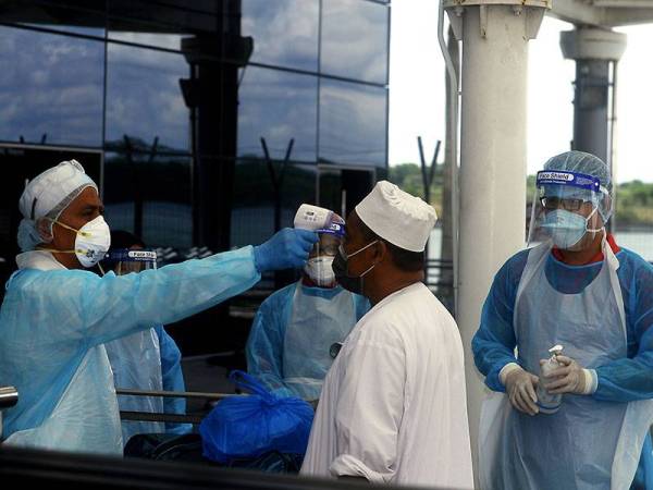 Petugas KKM memeriksa suhu badan jemaah Tabligh sebelum dikuarantinkan sebagai langkah mencegah penularan COVID-19. - Foto Bernama