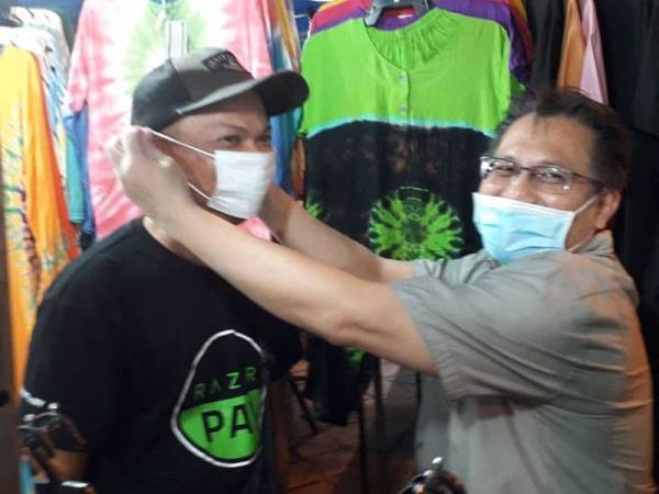 Nur Jazlan memakaikan pelitup mulut kepada seorang peniaga dalam Program Mesra Rakyat Bazar Karat Johor Bahru di Jalan Segget, Johor Bahru, malam tadi.