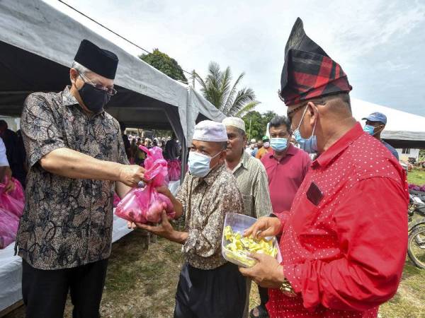 Annuar (kiri) mengagihkan daging korban kepada sebahagian penduduk pada Majlis Korban dan Mesra Adha Bersama Rakyat di Kampung Belukar Luas, Ketereh hari ini. - Foto Bernama