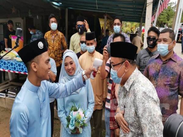 Pasangan pengantin, Nurul Haziqah Mohd Asri dan Muhammad Amirul Aizar Mohd Zawavi, 21, membuat pemeriksaan suhu ke atas calon Bebas, Amir Khusyairi Mohamad Tanusi. 