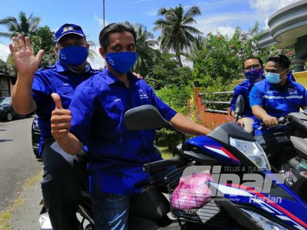 Mohd Zaidi (kiri) menggunakan motosikal bagi kempen rumah ke rumah di Kampung Klah Baru, Slim River hari ini.