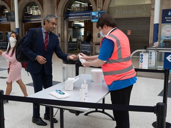 Seorang pekerja memicit cecair pembasmi kuman hand sanitizer kepada penumpang di Waterloo Station di London. - Foto AFP