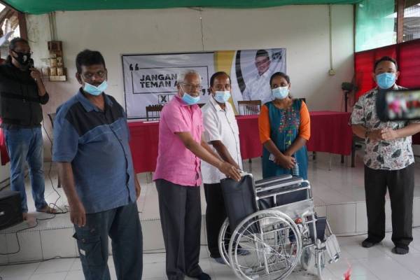 Sivanesan (dua dari kiri) dan Kula Segaran (tengah) menyerahkan kerusi roda untuk digunakan Munusamy sambil diperhatikan Amir Khusyairi ketika berkempen di Kampung Hendra Lama, kelmarin.