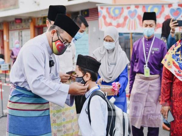 Amirudin memakaikan pelitup muka kepada seorang murid SRAI Seksyen 19 Shah Alam, hari ini.