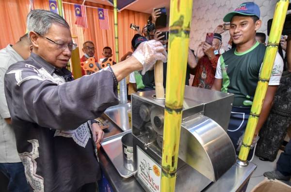 Mustapa (kiri) mencuba memerah tebu menggunakan mesin pemerah tebu milik peniaga Mohd Fadli Fauzi, 26, (kanan) pada Majlis Perasmian Kiosk Air Tebu Viral hari ini. -Foto Bernama