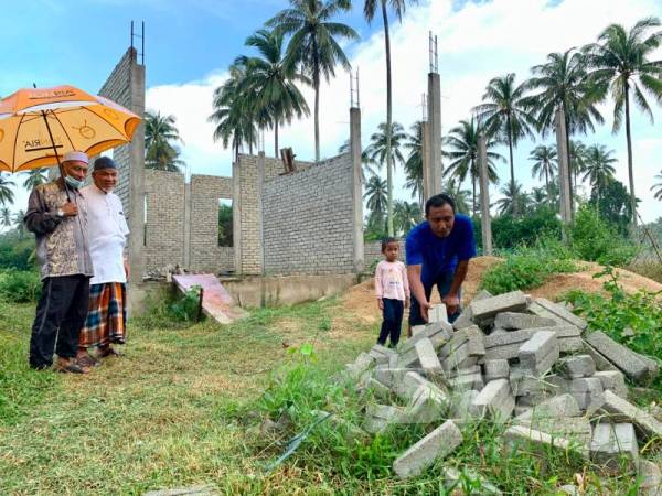 Tengku Mohd menyusun bata di hadapan tapak rumahnya yang masih terbengkalai sambil diperhatikan Abdul Rahman (kiri).