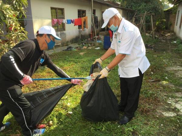 Hassan (kanan) membantu komuniti setempat membersihkan sampah dalam Program Gotong Royong Basmi Denggi di Kampung Orang Asli Kuala Masai, Pasir Gudang, hari ini.