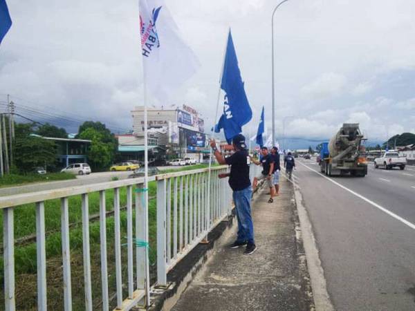 Shahre Sariman (tengah) bersama rakan Armada lain sedang melakukan kerja pemasangan bendera di tepi jalan Petagas, Putatan.