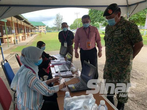 Muhammad Hafizuddeain (kanan) melawat proses pengundian awal yang dilaksanakan di Sekolah Agama Kem Lok Kawi, Putatan hari ini.