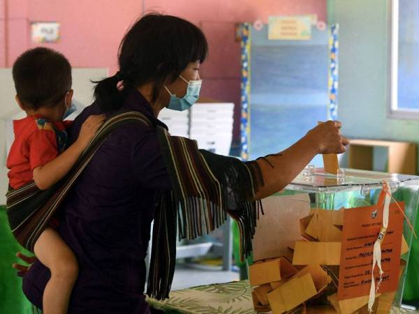 Pengundi Maitah Tandasai mengendong anak kecil semasa mengundi pada Pilihan Raya Negeri Sabah ke-16 di Sekolah Kebangsaan Mantob hari ini. - Foto Bernama