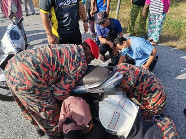 Anggota bomba cuba mengeluarkan tangan kiri mangsa yang tersepit di bahagian tayar belakang motosikal di Kampung Bahagia, Teluk Intan pagi tadi. - Foto ihsan bomba