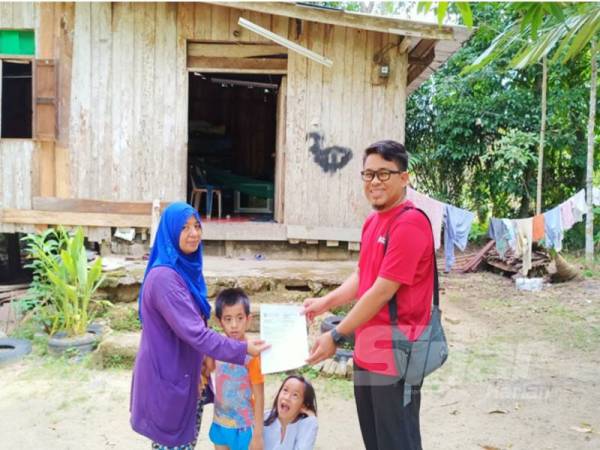 Muhammad Afiq Aiman (kanan) menyerahkan bil bayaran yang sudah dilangsaikan oleh Volunteer i-Care hasil sumbangan orang ramai kepada Wan Syarifah dan anak-anaknya