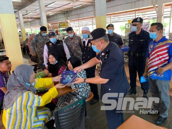 Ab Rashid (kanan) menyerahkan buku berkaitan amalan normal baharu kepada pengunjung Pasar Wakaf Bharu ketika melakukan operasi di sini hari ini.