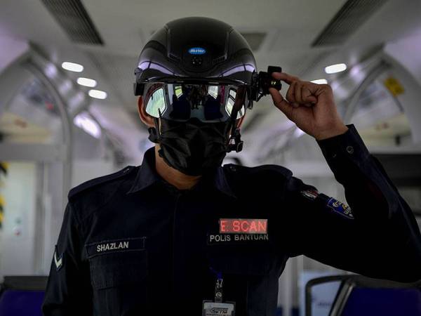 Anggota Polis Bantuan Kereta Api Tanah Melayu Berhad (KTMB) Muhd Amirul Shazlan Badrul Hisham melakukan rondaan di dalam tren menggunakan topi keledar pintar bagi mengesan suhu badan pengguna yang menggunakan perkhidmatan awam Kereta Api Tanah Melayu (KTM) ketika tinjauan hari ini. - Foto Bernama