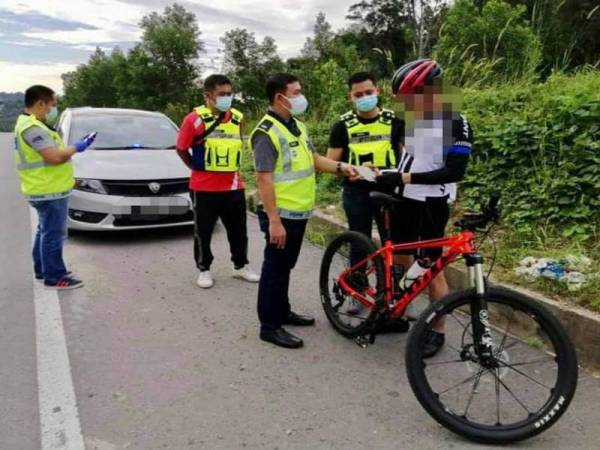 Mohd Haris (tiga dari kiri) mengenakan kompaun kepada individu yang berbasikal selepas didapati melanggar SOP PKPB di Jalan Papar Lama, Penampang.