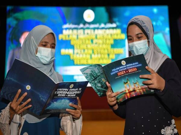 Kakitangan Bahagian Pembangunan Teknologi Maklumat Terengganu, Nur Nadhirah Abdul Manah (kanan) dan Nurharwani Mohd Harun melihat kandungan buku Pelan Induk Kerajaan Digital Pintar Terengganu 2021-2030 dan Pelan Strategik Taman Maya AI (Artificial intelligence) Terengganu 2021-2025 pada majlis pelancaran yang disempurnakan oleh Menteri Besar Terengganu Datuk Seri Dr Ahmad Samsuri Mokhtar di Wisma Darul Iman Hari ini. - Foto Bernama