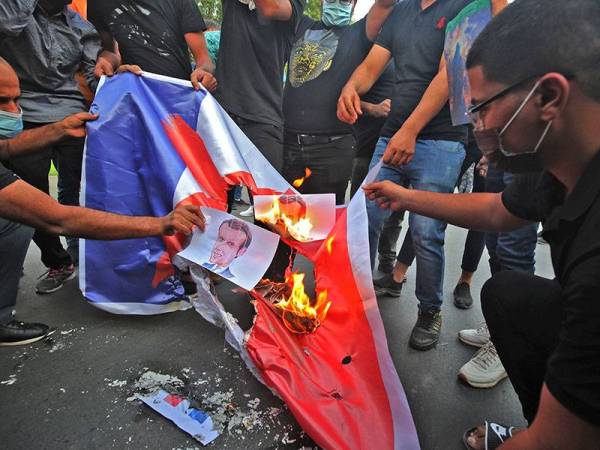 Penunjuk perasaan membakar poster Macron dan bendera kebangsaan Perancis ketika demonstrasi di hadapan Kedutaan Perancis di Baghdad, Iraq.