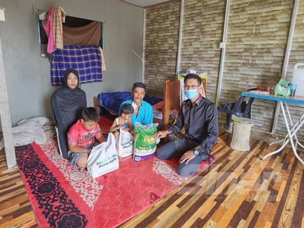 Ahmad Hambali (kanan) menyerahkan bantuan makanan asas ketika melawat Hamdi di Pokok Sena baru-baru ini.