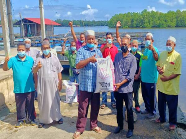 Wan Hassan (hadapan, kanan) menyerahkan sumbangan palet makanan ikan kepada Mustaffa yang mewakili Persatuan Penternakan Ikan Laguna Semerak (PPILS) di Laguna Semerak, Pasir Puteh.