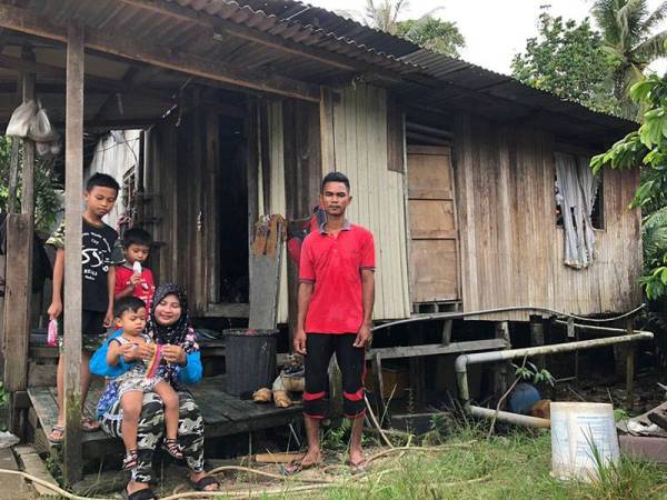 Siti Sarah dan Mohd Zulkhainain bersama tiga anak mereka, Mohd Hafiz Danial,11, (kiri) Mohd Shakir Darwish, 6, dan Mohd Dafi duduk di luar rumah pusaka yang menjadi tempat tinggal mereka di tepi tali air Kampung Cherang, Tanjung Mas, Kota Bharu.