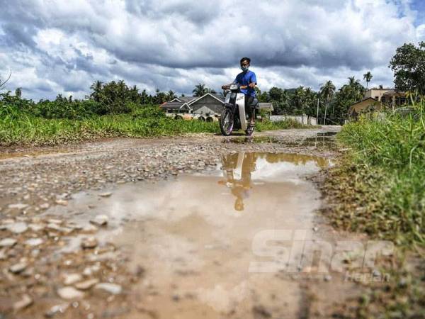 Seorang penduduk melalui jalan Kampung Hutan Palas, Kodiang di Kubang Pasu yang rosak dan berlubang.