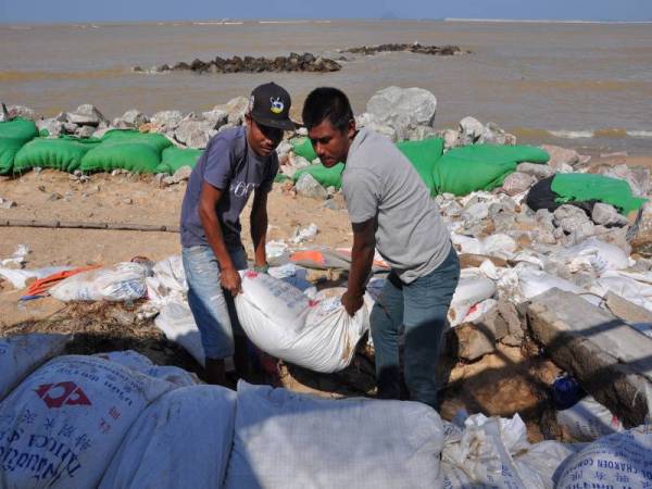 Mohd Azman Mohd Nafi, 30, (kanan) dan Abd Halim Ahmad, 34,(kiri) sedang meletakkan guni berisi pasir sebagai benteng pemecah ombak ketika tinjauan di Kampung Pengkalan Atap, Kuala Besut. - Foto Bernama