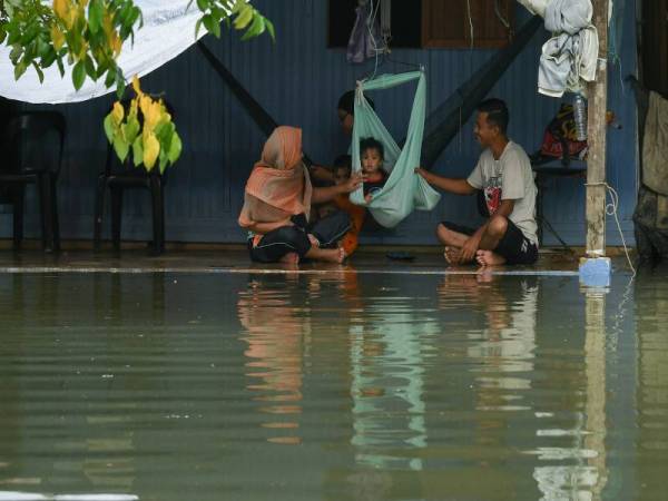 Mangsa banjir, Rozaiman Ibrahim, 34, (kanan) bersama isterinya Nor Ellham Mohamed, 31 (kiri), dan anak mereka, Aira Qhhaisara, 1, tengah) duduk di hadapan rumah ibu mereka yang dilanda banjir ketika tinjauan di Kampung Banggol. - Foto Bernama