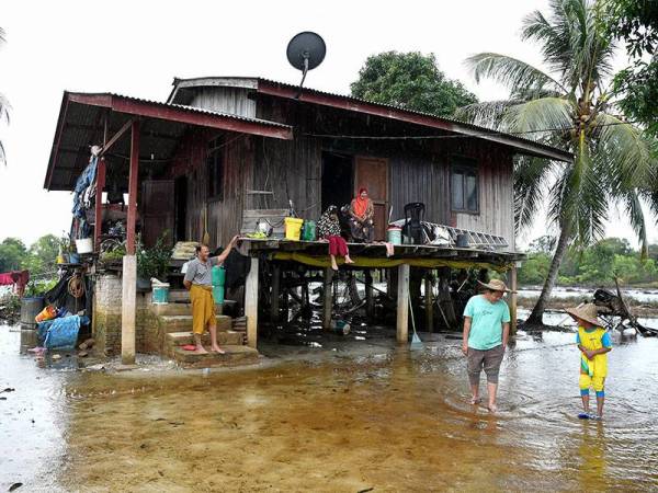 Mat Chek (kiri) bersama isteri melihat cucu mereka bermain air banjir termenung di hadapan rumah mereka di Kampung Padang Garam hari ini. - Foto Bernama