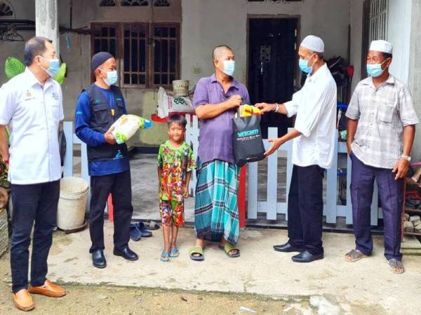 Mahadi (dua dari kiri) bersama Wan Hassan (dua dari kanan) menyampaikan bantuan makanan kepada 22 asnaf mangsa banjir di Kampung Gong Pasir, Pasir Puteh.